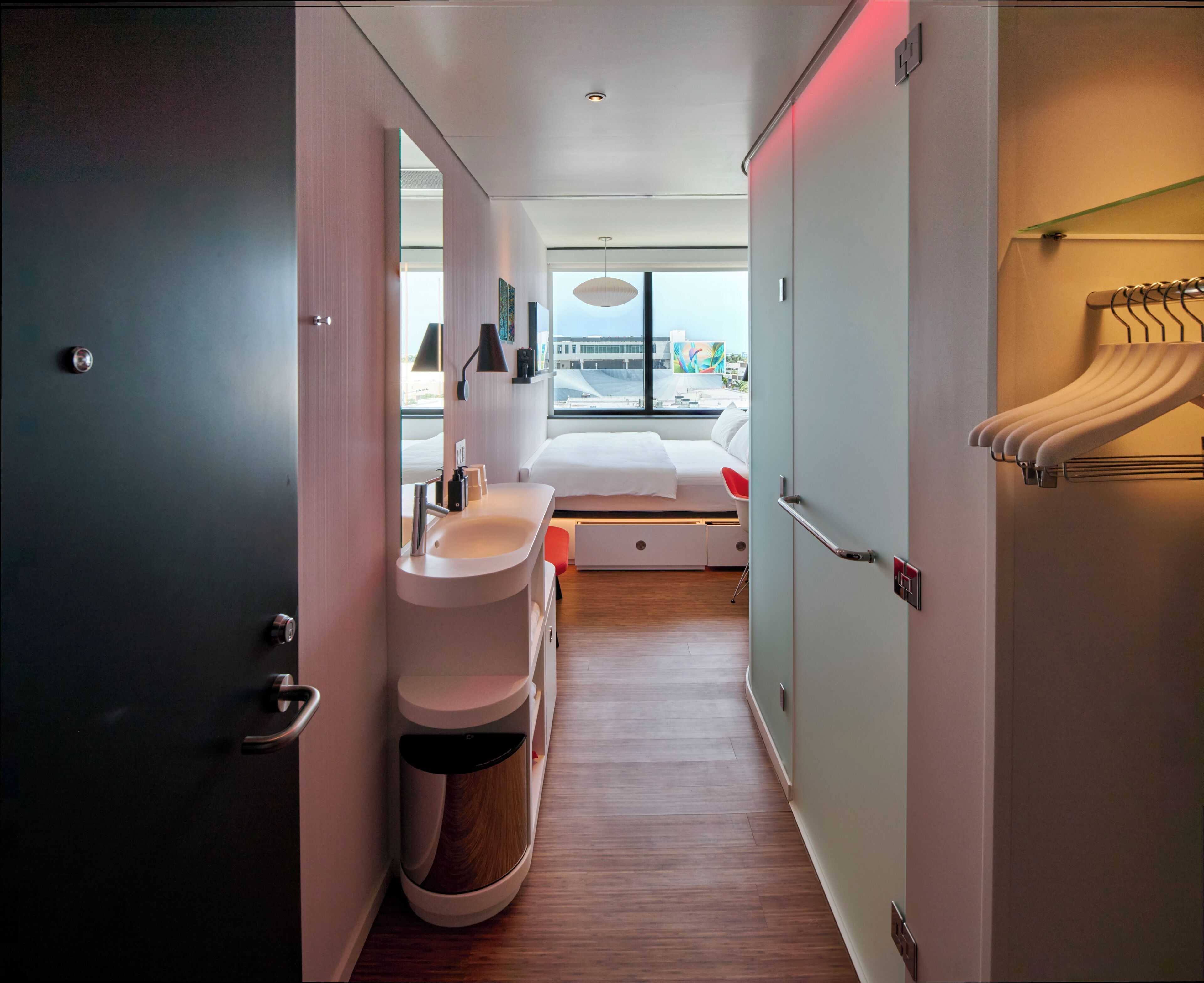 Une chambre d’hôtel moderne, dotée d’un lit, d’une table de chevet et offrant une vue sur la ville grâce à de grandes fenêtres.