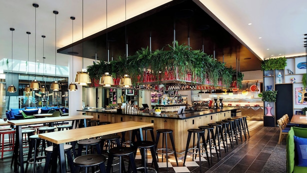 A modern bar area with high stools, a central bar counter, and hanging plants. - citizenM Miami South Beach (Miami Beach)