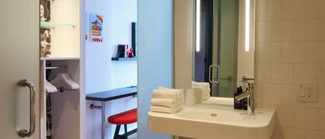 Un baño moderno con cabina de ducha de vidrio, un lavamanos blanco con espejo y un banco rojo.
