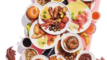 Variedad de alimentos para el desayuno dispuesta sobre una mesa, incluyendo tostadas, huevos, salchichas y frutas.