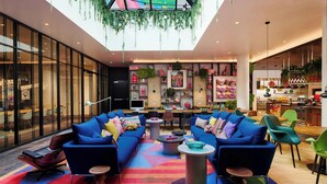 A modern lounge area with blue sofas, colorful rugs, and a variety of plants and decorative items on shelves. - citizenM Miami South Beach (Miami Beach)