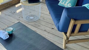 Une terrasse en bois avec un canapé bleu, une petite table sur laquelle se trouve un ordinateur portable, une plante en pot et une vue sur la plage.