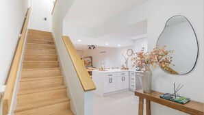 A modern kitchen with white cabinets, a wooden staircase, and a mirror on the wall. - Gorgeous Beach Front Condo, Near Flagler Ave - 701 (New Smyrna Beach)