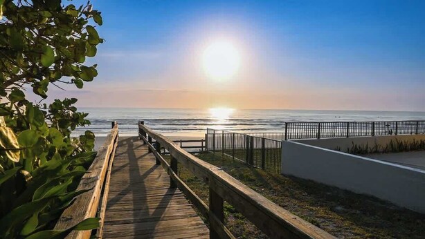 A wooden boardwalk leading to a beach with a fence and a clear view of the ocean. - Gorgeous Beach Front Condo, Near Flagler Ave - 701 (New Smyrna Beach)