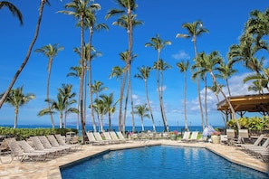 A poolside area with lounge chairs and palm trees, overlooking the ocean.