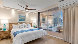 Una habitación de hotel con una cama grande, un ventilador de techo, un balcón con vistas y un equipo de aire acondicionado.