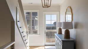 Un couloir avec un escalier, une porte donnant sur un balcon et une console surmontée de lampes.