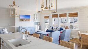 Une cuisine moderne avec des meubles blancs, un grand îlot central doté d’un évier et un coin repas avec des chaises en osier.
