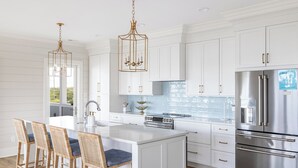 Une cuisine moderne avec des meubles blancs, des appareils en acier inoxydable et un îlot central doté de tabourets de bar.