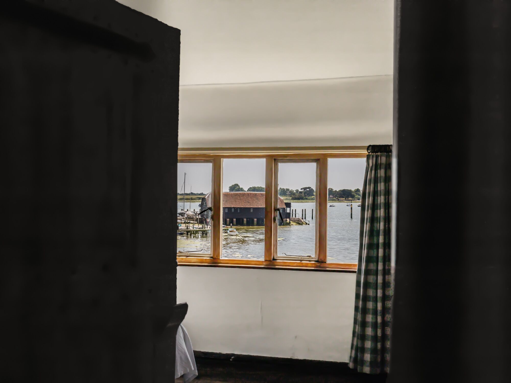 A room with a large window overlooking a dock and water, a wooden door, and a curtain.