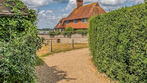 Une maison traditionnelle en pierre, avec un toit de tuiles, entourée de haies bien entretenues et d’un chemin de gravier menant à l’entrée.