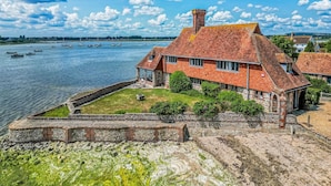 Une maison située sur la côte, dotée d’un mur en pierre et d’une pelouse verdoyante, et offrant une vue sur une étendue d’eau où se trouvent des bateaux.