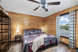 Ein Schlafzimmer mit einem Bett, einem Deckenventilator, einem Fenster mit Vorhängen und einer Holzwand.