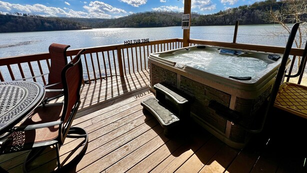 Een houten terras met een jacuzzi, een tafel en stoelen met uitzicht op een meer.