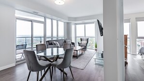 Una sala de estar moderna con una mesa de comedor de vidrio, sofás grises y un ventanal con vistas a la ciudad.