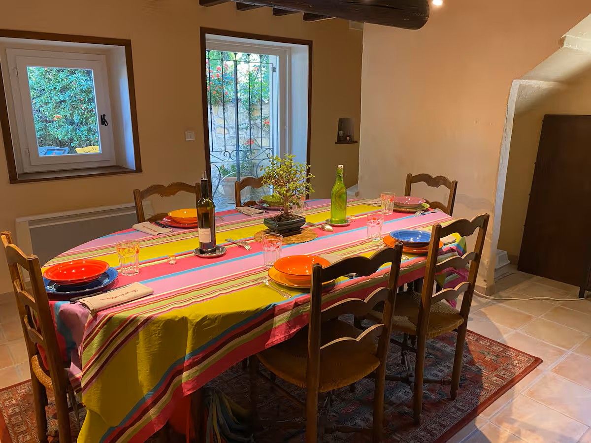 Une table à manger dressée avec une nappe colorée, des assiettes et des verres, entourée de chaises.