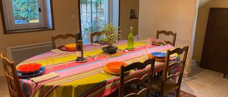 Une table à manger dressée avec une nappe colorée, des assiettes et des verres, entourée de chaises.