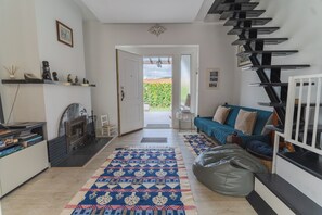 A modern living room with a fireplace, a blue sofa, a patterned rug, and a staircase. - Belas Rustic Chick (Belas)