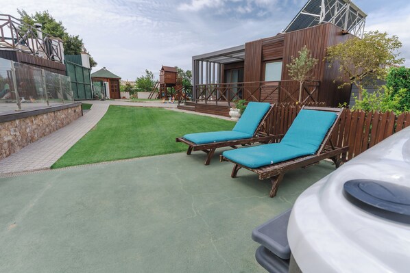 A patio area with two wooden lounge chairs, a white car, and a green lawn. - Belas Rustic Chick (Belas)