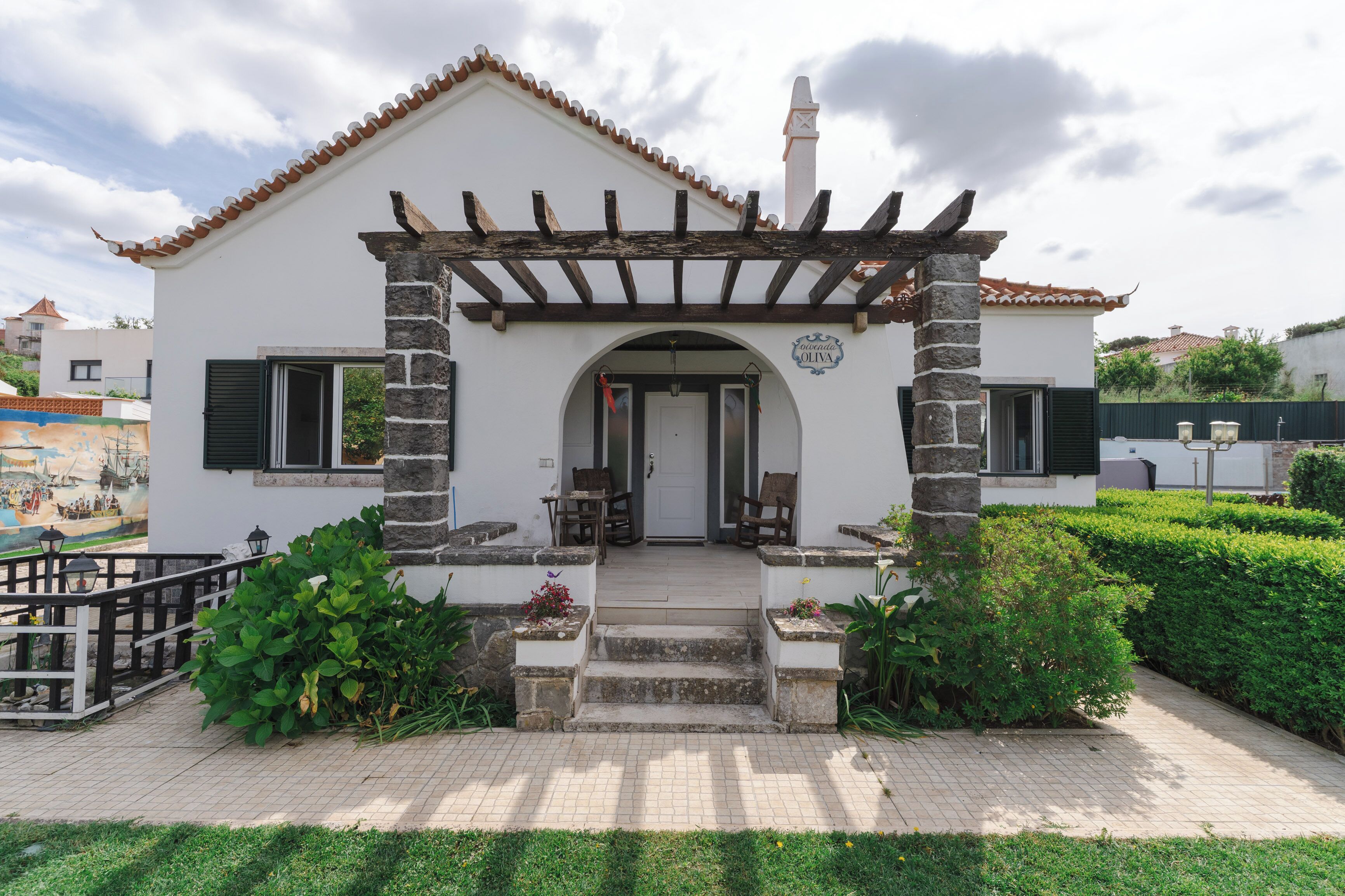 A building with a white facade, a stone pillar, and a wooden pergola.