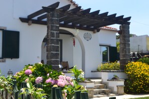 A building with a white facade, a wooden pergola, and a stone column. - Belas Rustic Chick (Belas)