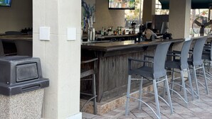An outdoor bar area with a counter, bar stools, and a television screen displaying a program.