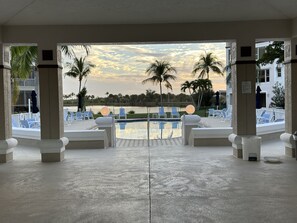 A pool area with lounge chairs and palm trees, viewed through an open doorway. - A Wave From it All: Unbelievable amenities and 4 miles to beach! (Fort Myers)