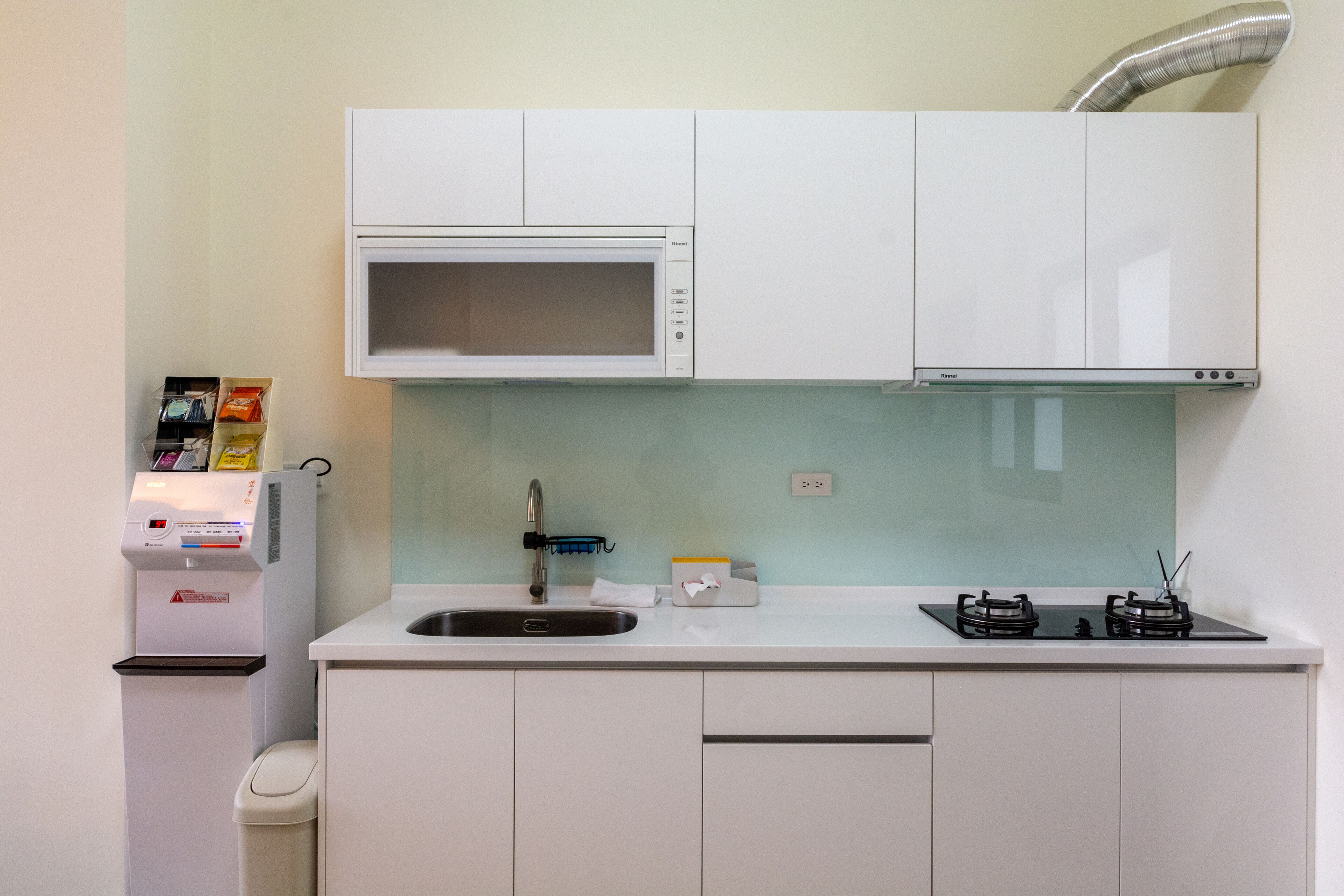 Een kleine keuken met een magnetron, spoelbak en gasfornuis.