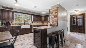 A kitchen with dark wood cabinets, a granite countertop, and a brick accent wall. There is a bar area with stools and a coffee station.