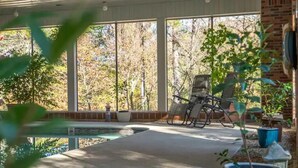 A covered patio with a pool, chairs, and potted plants.