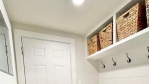 A hallway with a white door, a bench with cushions, and shelves with baskets and hooks. - Lakeside in Muskoka (Huntsville)