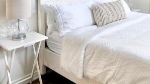 A neatly arranged bedroom with a white bed, two bedside tables, and a wall-mounted light fixture. - Lakeside in Muskoka (Huntsville)