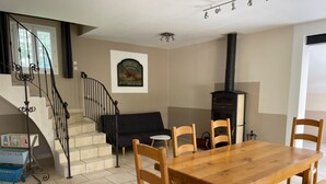 Un'area pranzo con un tavolo e sedie in legno, un divano nero, una scala con ringhiera in ferro battuto e un camino.