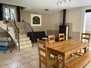 Ein Essbereich mit einem Holztisch und Stühlen, einer schwarzen Couch, einer Treppe mit schmiedeeisernem Geländer und einem Kamin.