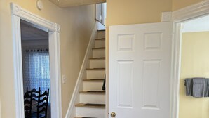 A staircase leading to a second floor, a white door with a doorknob, and a dining area with chairs and a table.