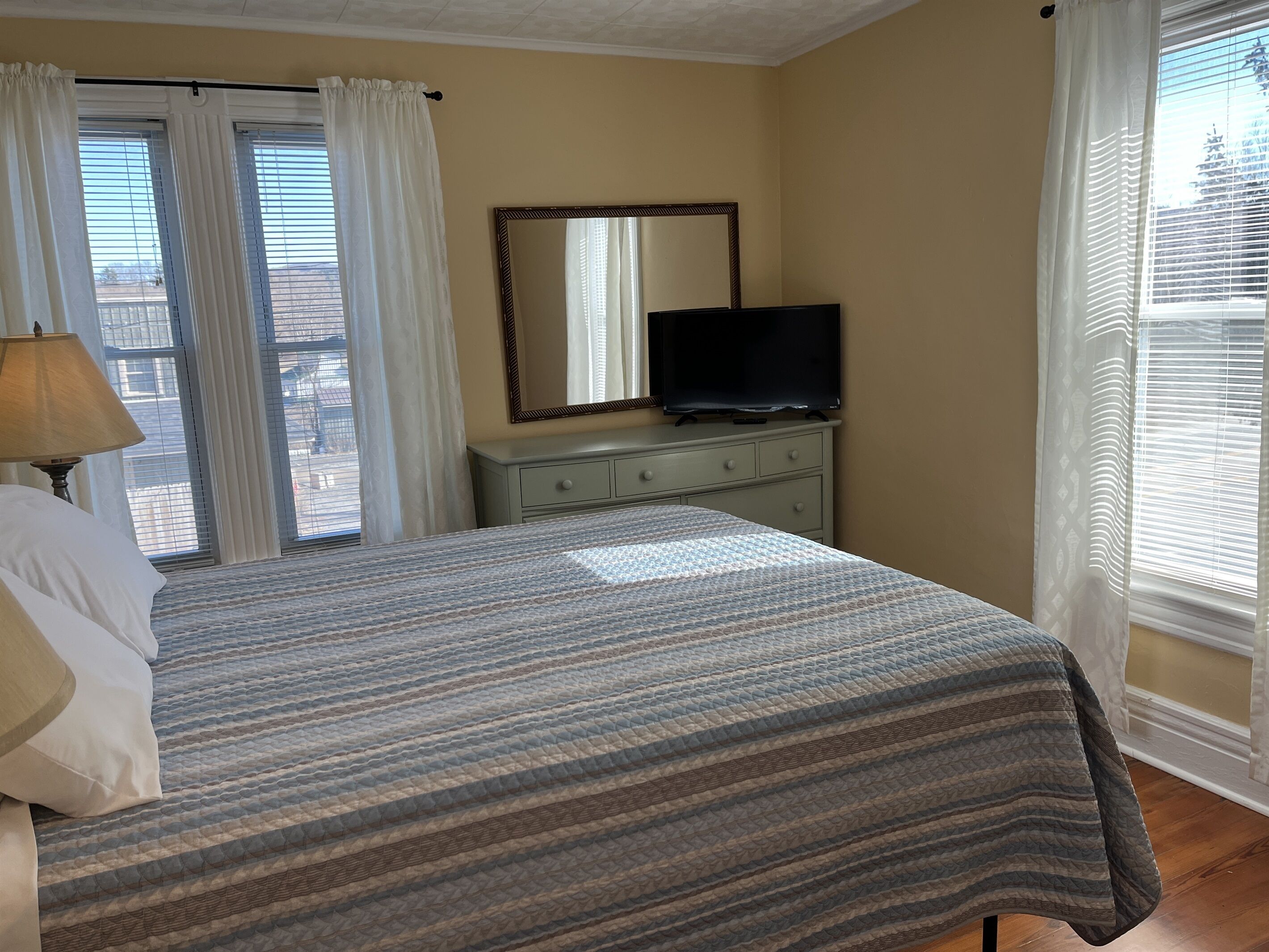 Une chambre d’hôtel avec un lit, une commode, une télévision et une fenêtre avec des rideaux.