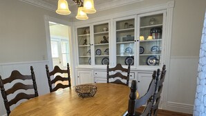 A dining room with a round wooden table, six wooden chairs, and a white cabinet with glass doors displaying dishes.