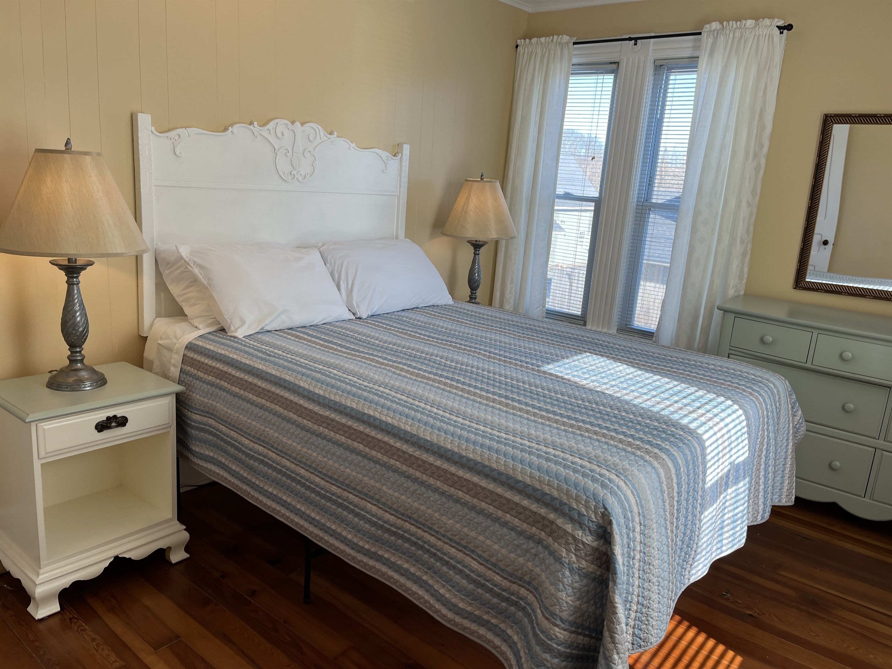 A bedroom with a bed, nightstands, a dresser, and a window with curtains.