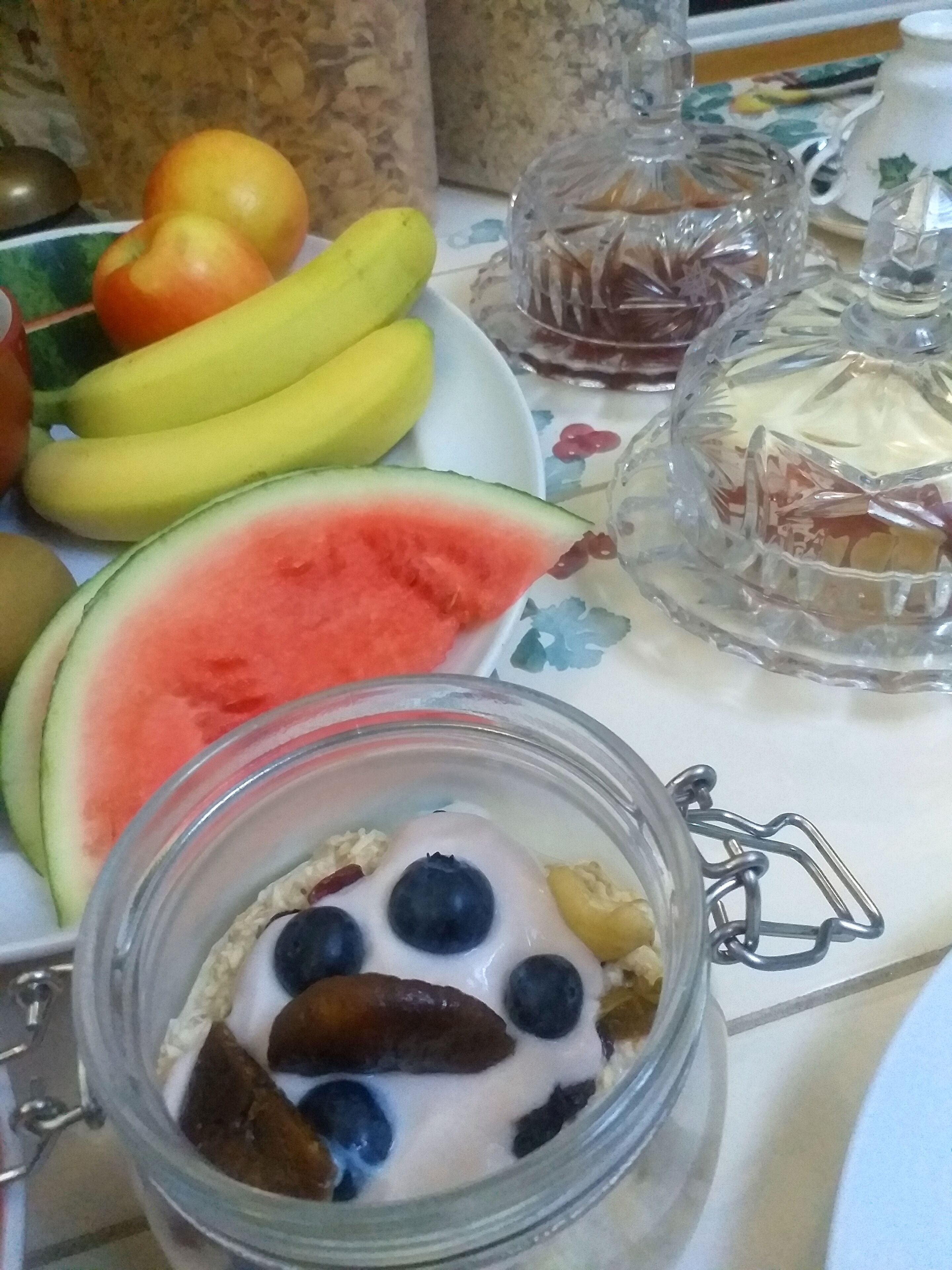 A table with a plate of fruits, a glass jar with yogurt and berries, and a decorative glass container.