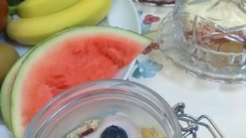 Una mesa con un plato de frutas, un tarro de vidrio con yogur y bayas, y un recipiente de vidrio decorativo.