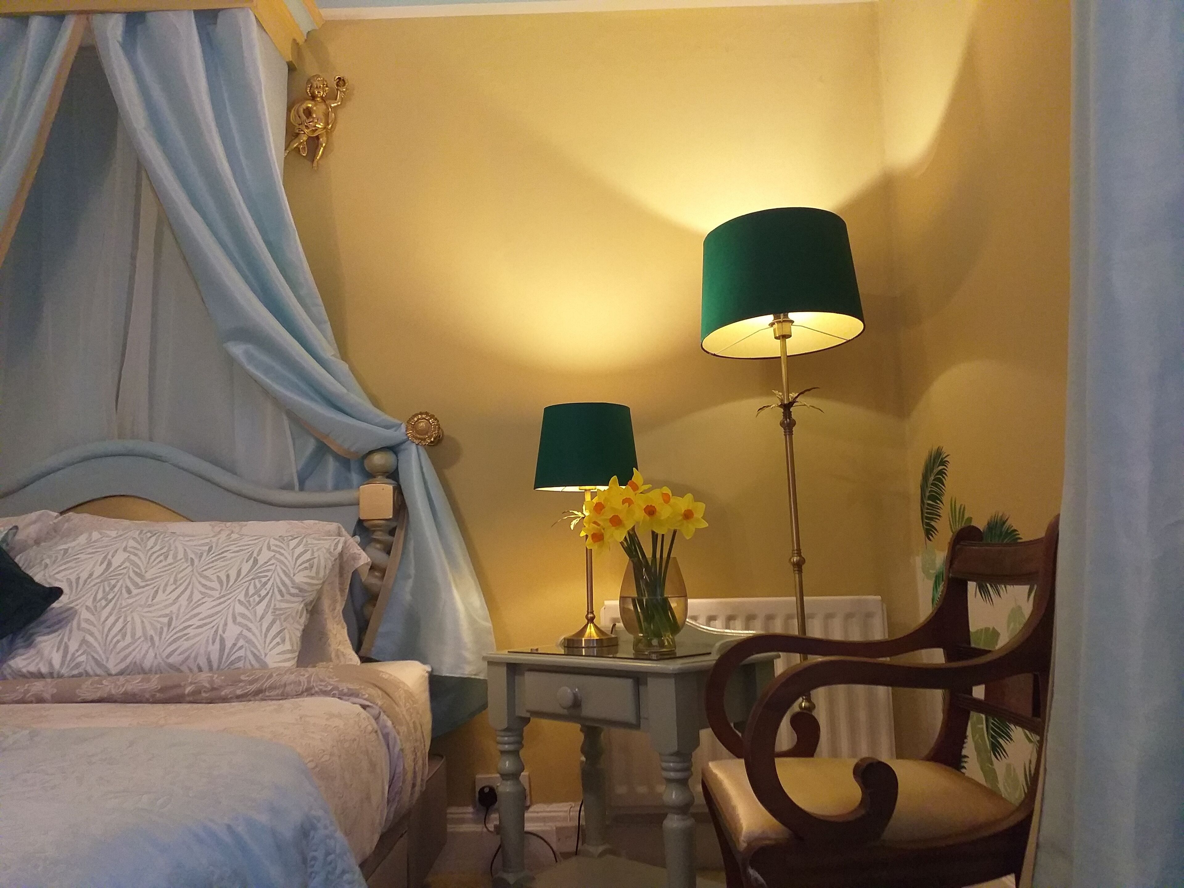 Une chambre à coucher avec un lit à baldaquin, deux lampes de chevet, une table de chevet, une chaise et un radiateur.