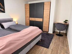 Un dormitorio con cama, armario, escritorio y silla.