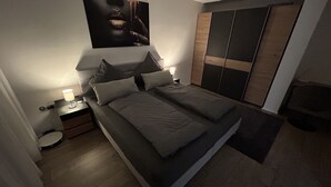 A modern bedroom with a bed, nightstands, a lamp, a wardrobe, and a painting on the wall.