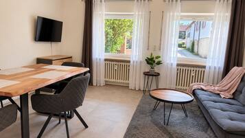 Een moderne woonkamer met een eethoek, een bank, een aan de muur bevestigde televisie en uitzicht op het buiten.