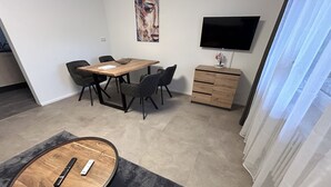 A modern room with a wooden dining table, four chairs, a TV mounted on the wall, and a small wooden cabinet.
