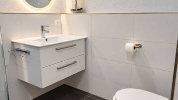 Un bagno moderno con un mobile lavabo bianco, uno specchio rotondo illuminato, un water e un cestino.