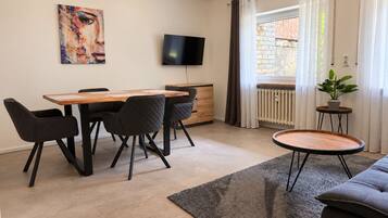 Ein modernes Wohnzimmer mit Essbereich, einem Flachbildfernseher, einer Topfpflanze und Blick ins Freie.