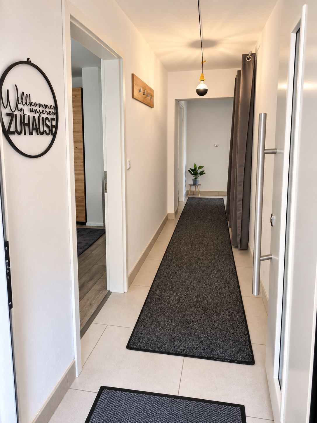 A hallway with a dark carpet, a welcome sign, a pendant light, and a door with a handle.