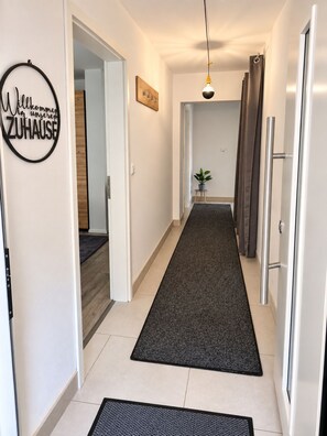 A hallway with a dark carpet, a welcome sign, a pendant light, and a door with a handle.