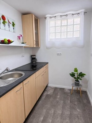 A kitchen with a sink, countertop, cabinets, a coffee maker, a window with curtains, and a small potted plant.